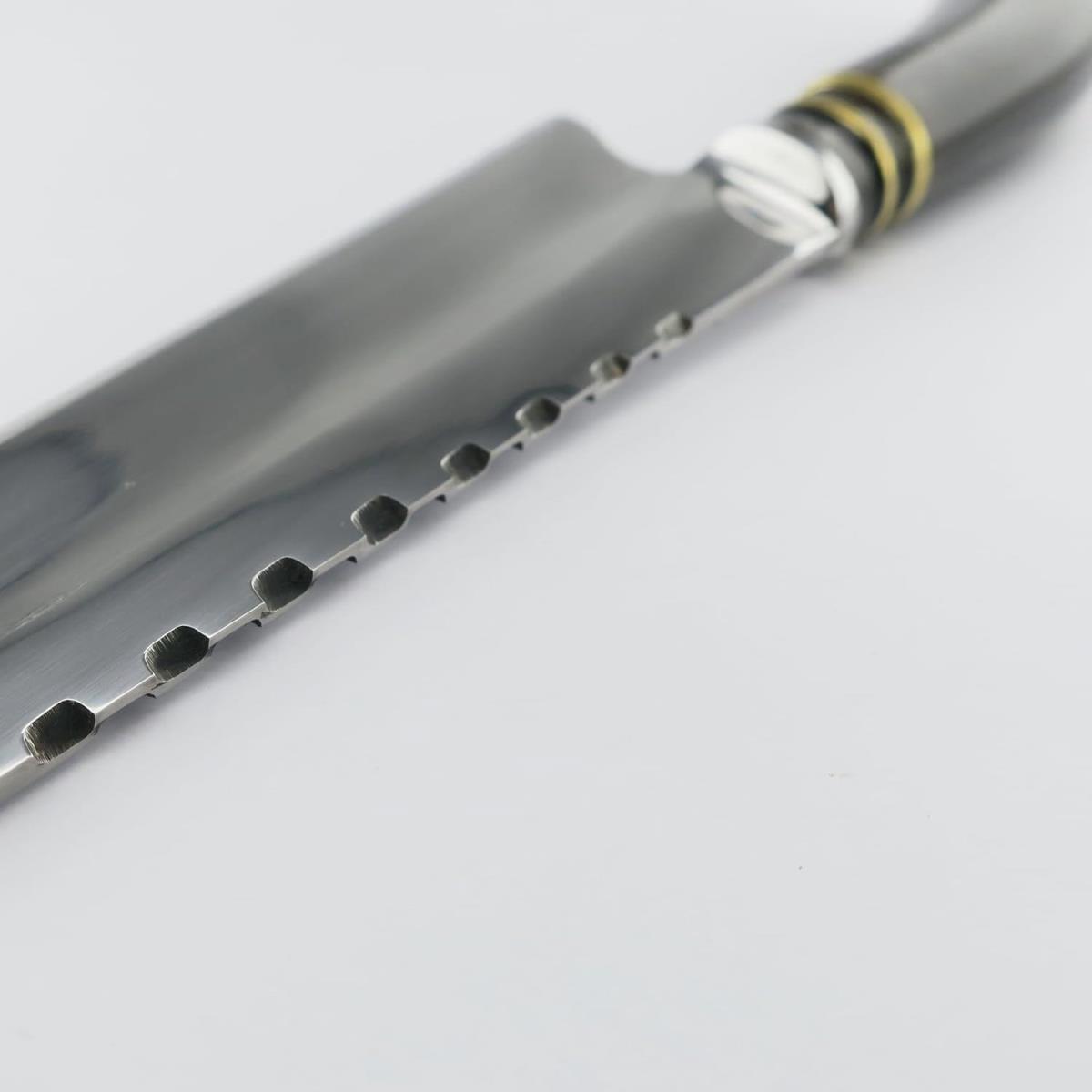 Primer plano de un cuchillo de acero inoxidable Vaca 7.1in Oscuro, con una elegante hoja plateada con hendiduras únicas a lo largo del lomo y un mango con detalles dorados y plateados, ideal para tareas de cocina.