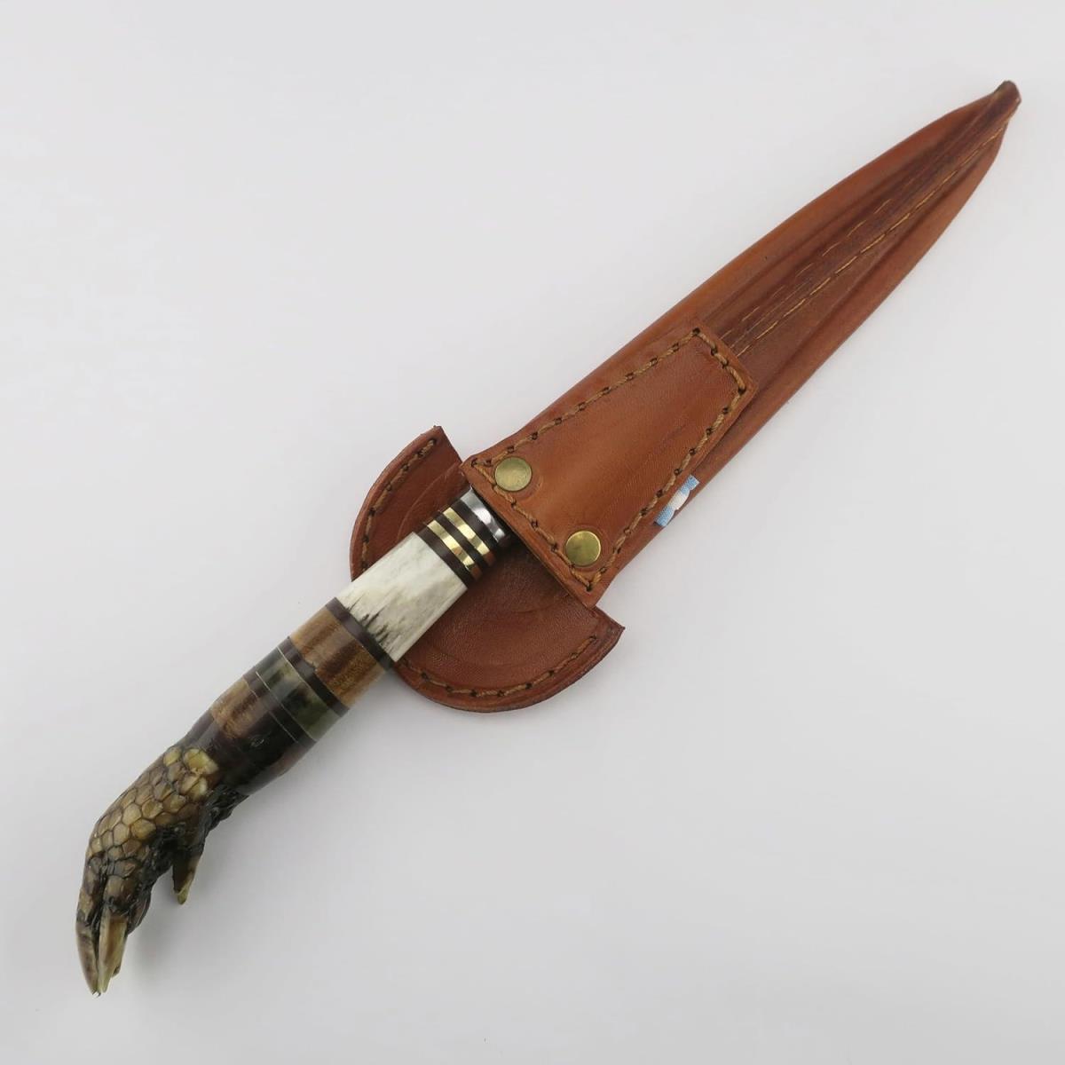 Cuchillo exótico con mango de garra de armadillo y hoja de acero inoxidable, con anillos decorativos y funda de cuero marrón. Ideal para coleccionistas o regalos únicos.
