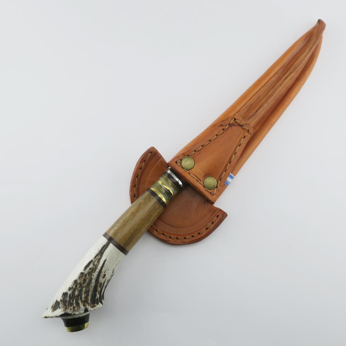 Cuchillo de acero inoxidable con mango de asta de ciervo, detalles rústicos de madera y adornos de latón, guardado en una funda de cuero marrón cosida. Ideal para caza, camping o coleccionismo, reflejando artesanía tradicional y durabilidad.