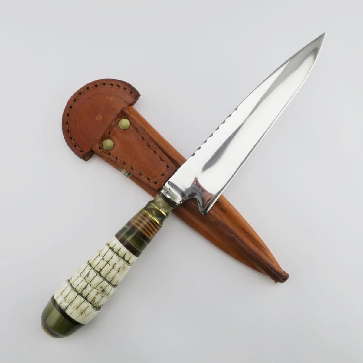 Cuchillo de caza con hoja de acero inoxidable y mango artesanal de cola de armadillo, incluye funda de cuero marrón a juego sobre un fondo blanco.